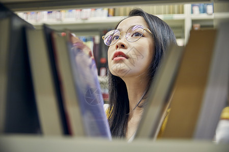 年轻女学生在图书馆找书背景图片