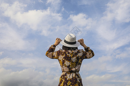 手扶草帽看着天空的时尚美女背影背景图片