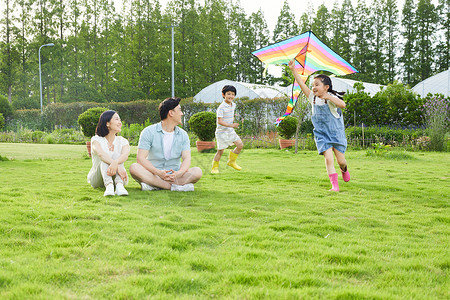 年轻夫妻看着孩子追逐玩风筝高清图片