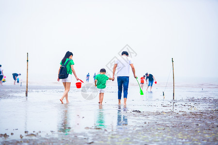 海边游玩一家三口在退潮滩涂上背景