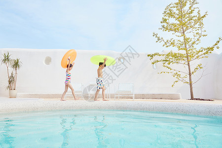 小男孩和小女孩拿着游泳圈在泳池边行走兄妹高清图片素材