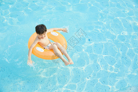 小男孩游泳小男孩躺在泳池里的游泳圈上背景
