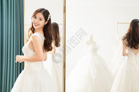 在镜子前试穿婚纱的甜美新娘背景图片