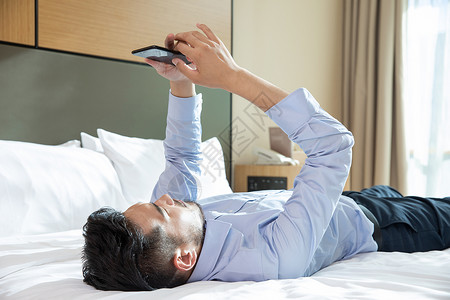 商务男性躺在酒店床上看手机职业男性高清图片素材