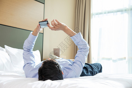 商务男性躺在酒店床上看手机职业装高清图片素材