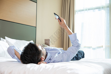 商务男性躺在酒店床上看手机商务出行高清图片素材