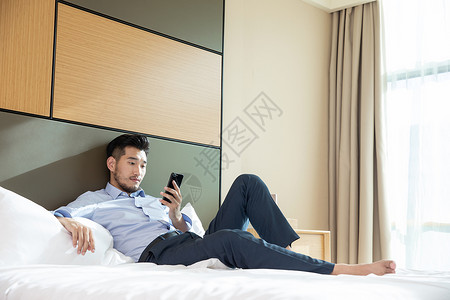 商务男性躺在酒店床上看手机商旅高清图片素材