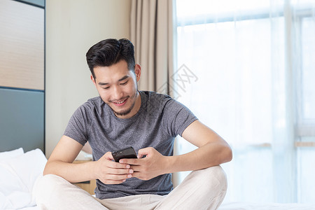 青年男性坐在酒店床上看手机背景图片