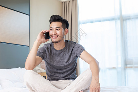青年男性坐在酒店床上打电话背景图片