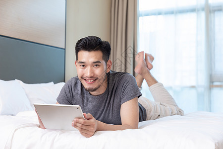 商务男性趴在酒店床上玩平板电脑背景图片