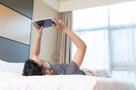青年男性躺在酒店床上玩平板电脑背景图片