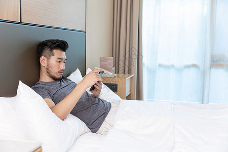 商务男性躺在酒店床上看手机差旅高清图片素材