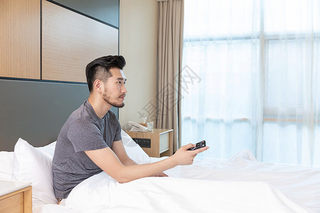 男性躺在酒店床上看电视图片素材