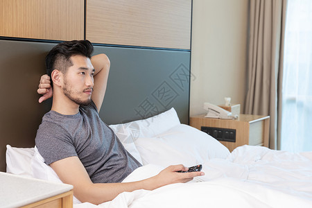 男性躺在酒店床上看电视背景图片
