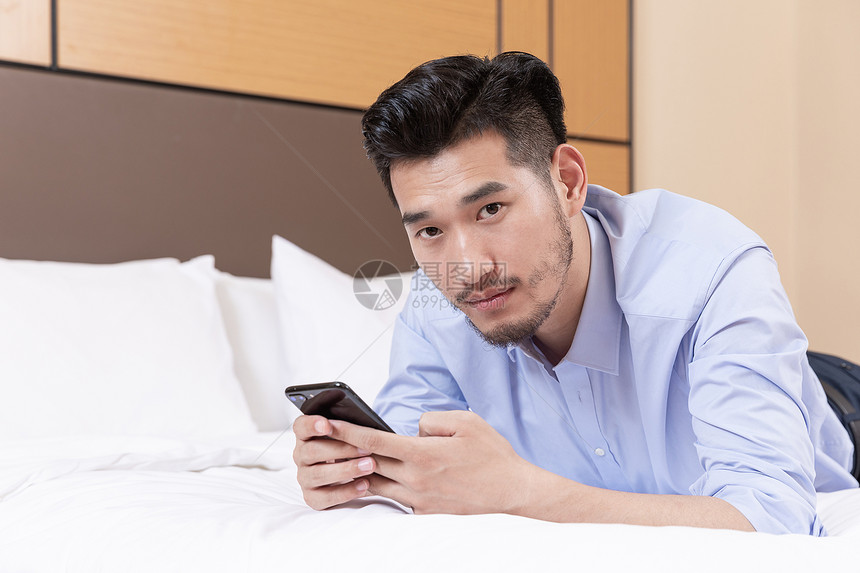 职业男性酒店出差趴床上玩手机图片