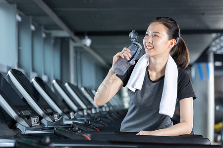 趴在跑步机上休息喝水的健身女性图片