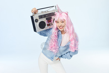 漂亮的烫发夹板录音机放在肩膀上单手叉腰的时尚粉色长发美女背景