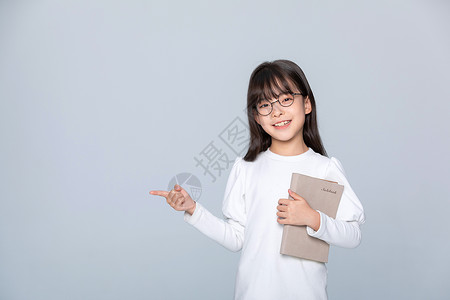 小女孩抱着练习本站着手指旁边背景图片