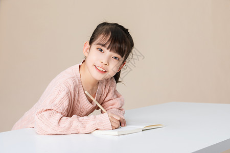 坐在笔上的女孩小女孩趴在桌子上写字做作业背景