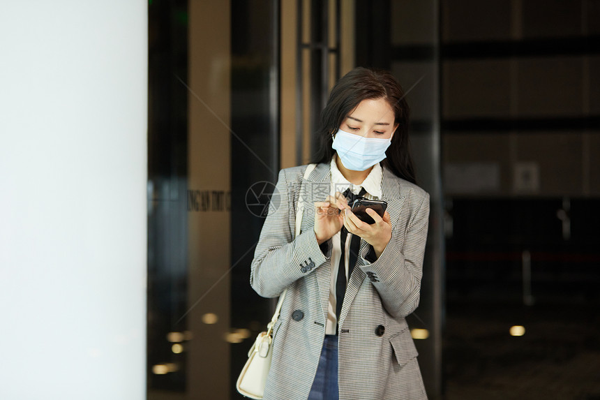 戴口罩的女白领下班低头玩手机图片