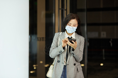 戴口罩的女白领下班低头玩手机高清图片