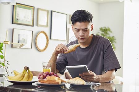 年轻男士吃早餐看平板电脑背景图片