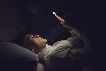 躺床上玩手机年轻男士深夜躺在床上玩手机背景
