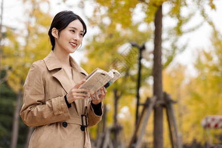 风衣女知性女青年手捧书本户外阅读背景