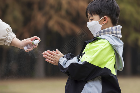 秋冬小男孩疫情期间逛公园手部消毒高清图片