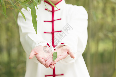 穿着练功服的女性手里捧着一片竹叶背景图片