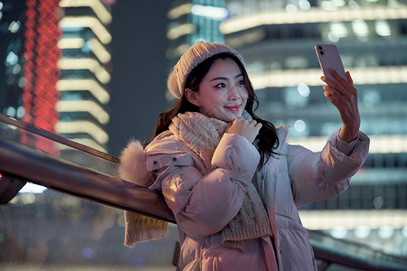 手机美颜夜晚使用手机自拍的冬季女性背景