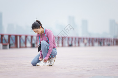 添衣保暖女性半蹲在跑道上系鞋带背景