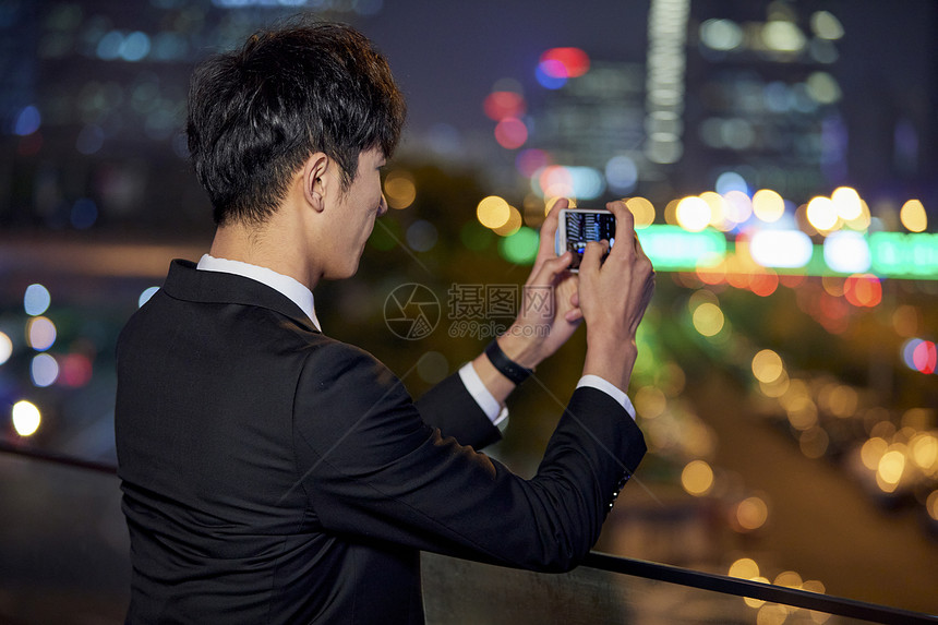 商务男青年用手机拍摄城市夜景图片
