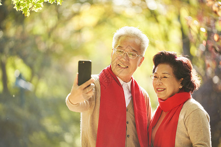 老年夫妇公园里用手机自拍秋天高清图片素材