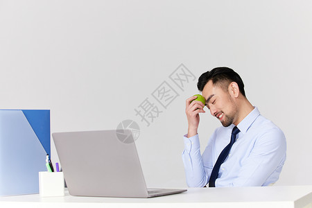 男性拿着青苹果坐在办公桌前图片