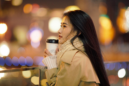 冬季夜晚都市女性手握咖啡杯侧脸人像背景图片