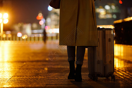 夜晚都市女性手提行李箱走在路上高清图片