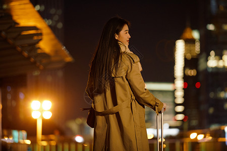 夜晚都市女性手提行李箱走在路上高清图片