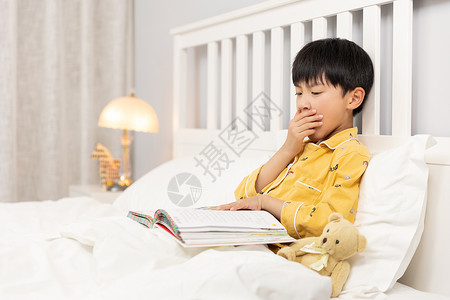 犯困小孩在床上看书犯困的小男孩背景