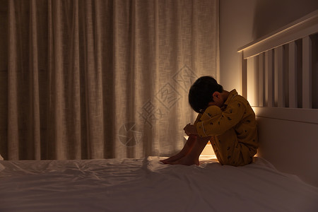 小男孩一个人蜷缩在床角高清图片