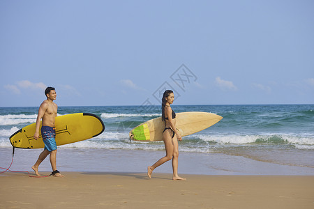 冲浪的情侣年轻男女手拿冲浪板海边行走背景