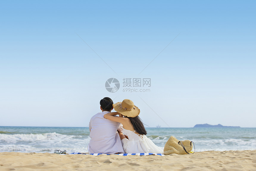 年轻情侣夏日坐在沙滩看海背影图片