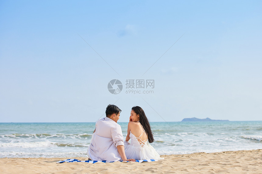 年轻情侣坐在沙滩对视背影图片