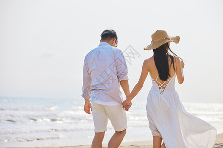年轻情侣牵手海边散步背影背景图片
