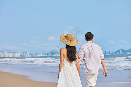 年轻情侣牵手海边散步背影背景图片