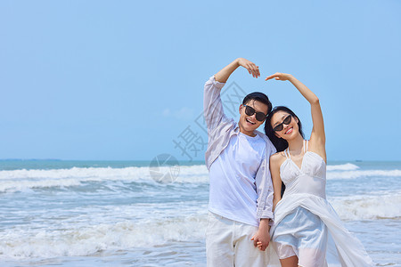 年轻女性比心夏日海边情侣比爱心背景