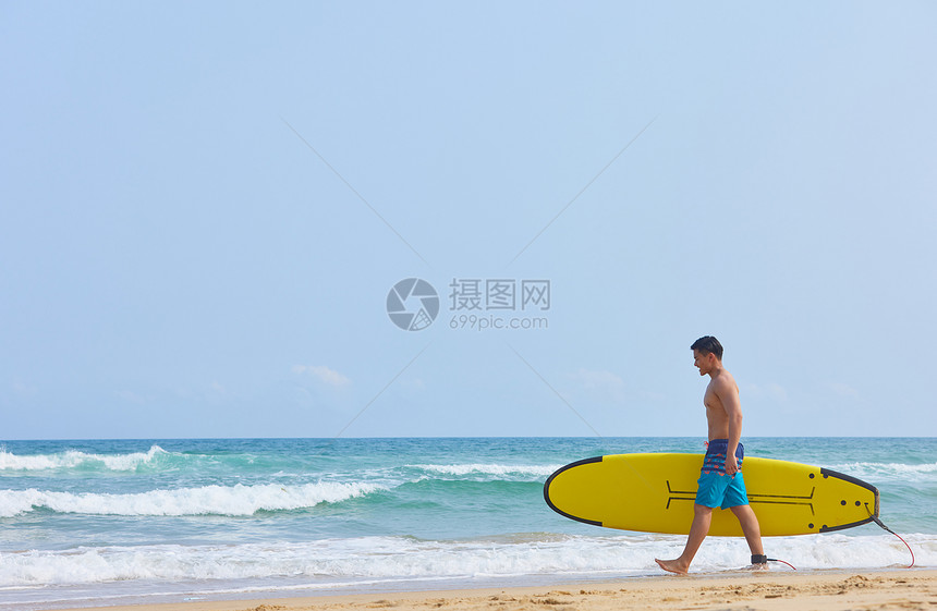 年轻男士拿着冲浪板海边行走图片