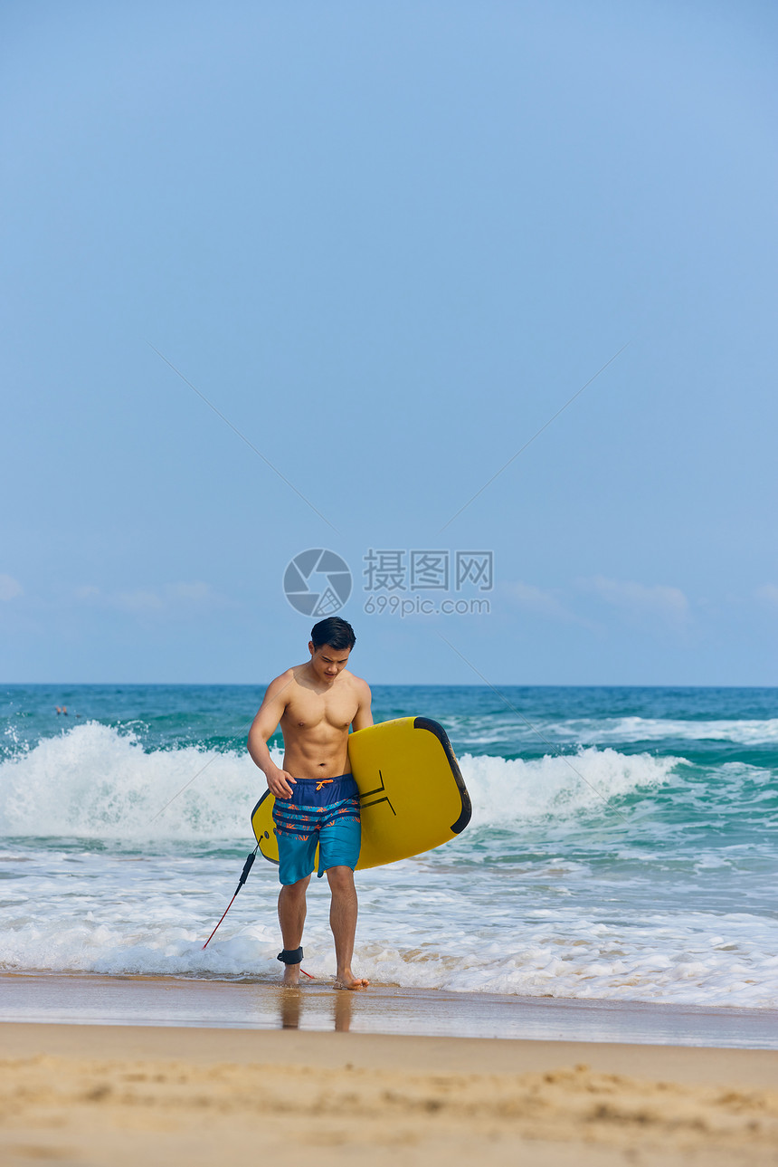 年轻男士拿着冲浪板海边行走图片