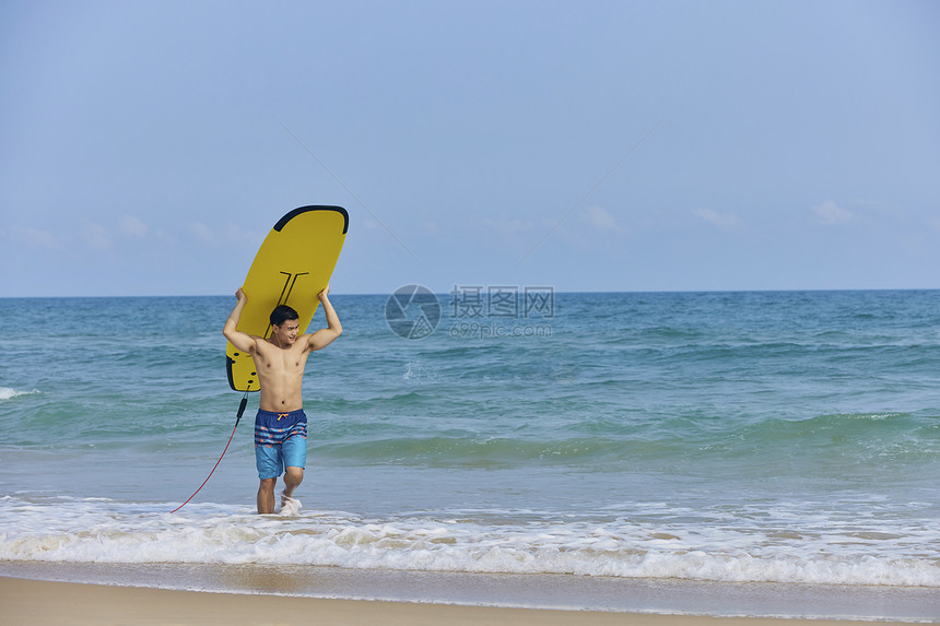 年轻男士举着冲浪板走向岸边图片