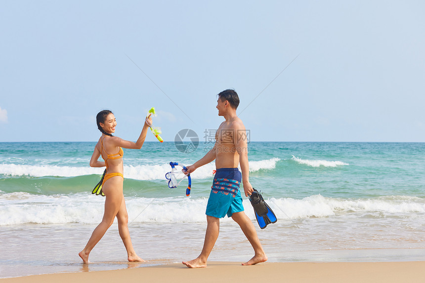 年轻情侣拿着潜水装备海边行走图片